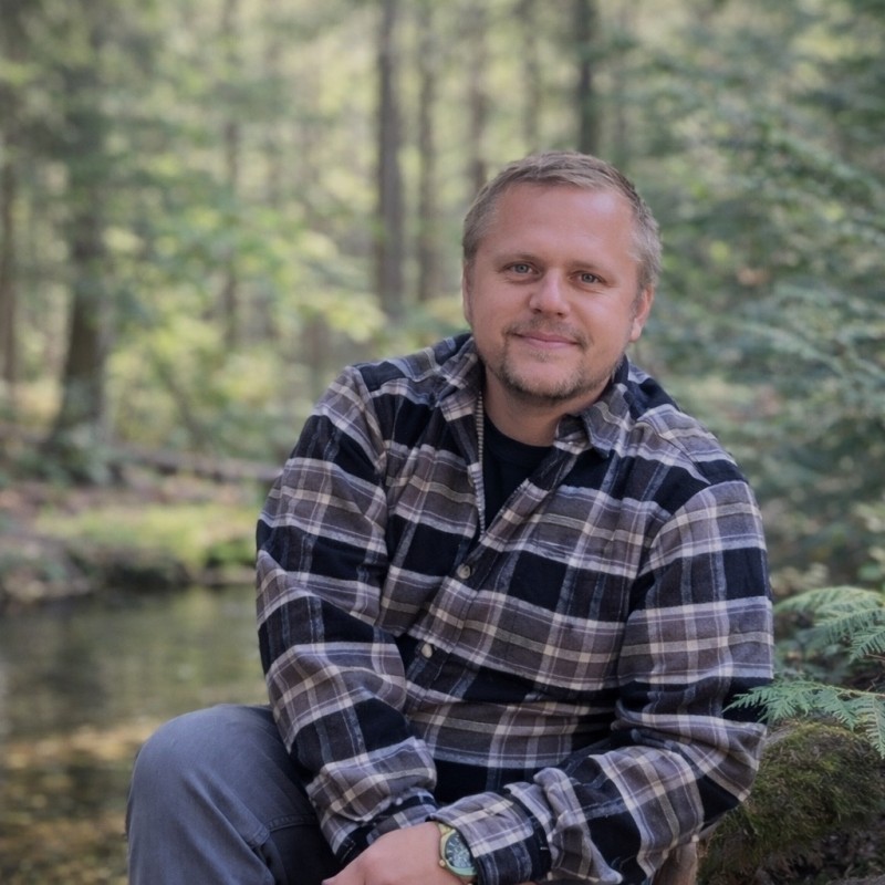 Shane Sipple seated beside a forest creek